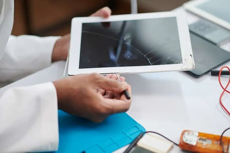 Hands repairing a white tablet with a severely cracked touch screen.