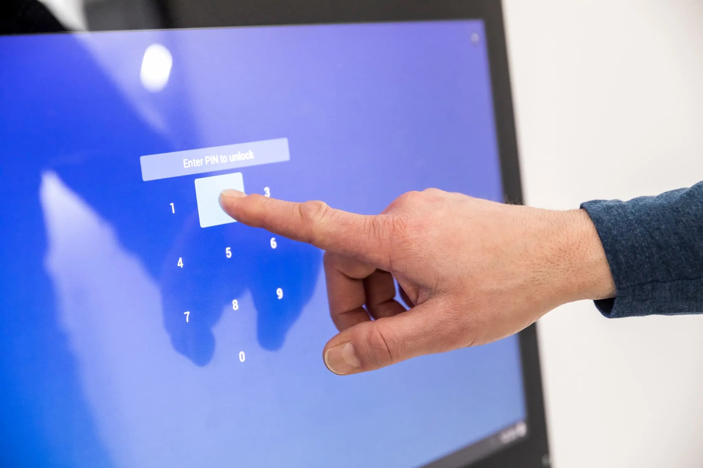 Hand entering a PIN on a blue commercial touch screen monitor.