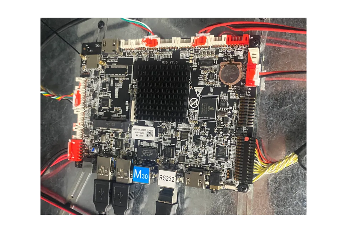 Close-up of a dark circuit board with various chips, ports, and red/black wires, essential for touch technology.