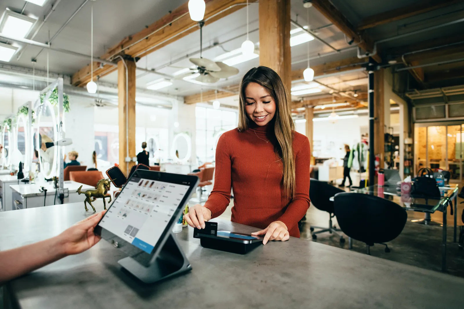 Smiling woman paying with a credit card at a modern POS system in a salon.