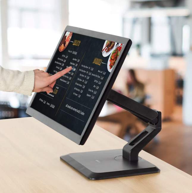 Hand interacting with a black touchscreen menu displaying food items on a wooden counter.
