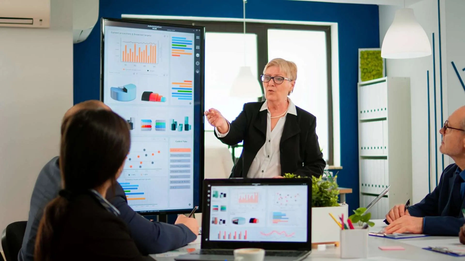 Businesswoman presenting data on a large 4K touch screen monitor to colleagues in a modern office.