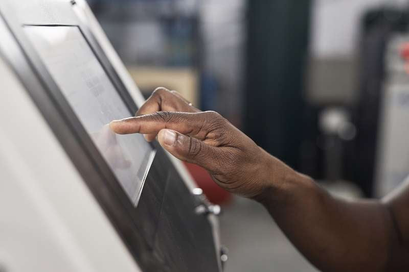 Hand operating an industrial touchscreen control panel.