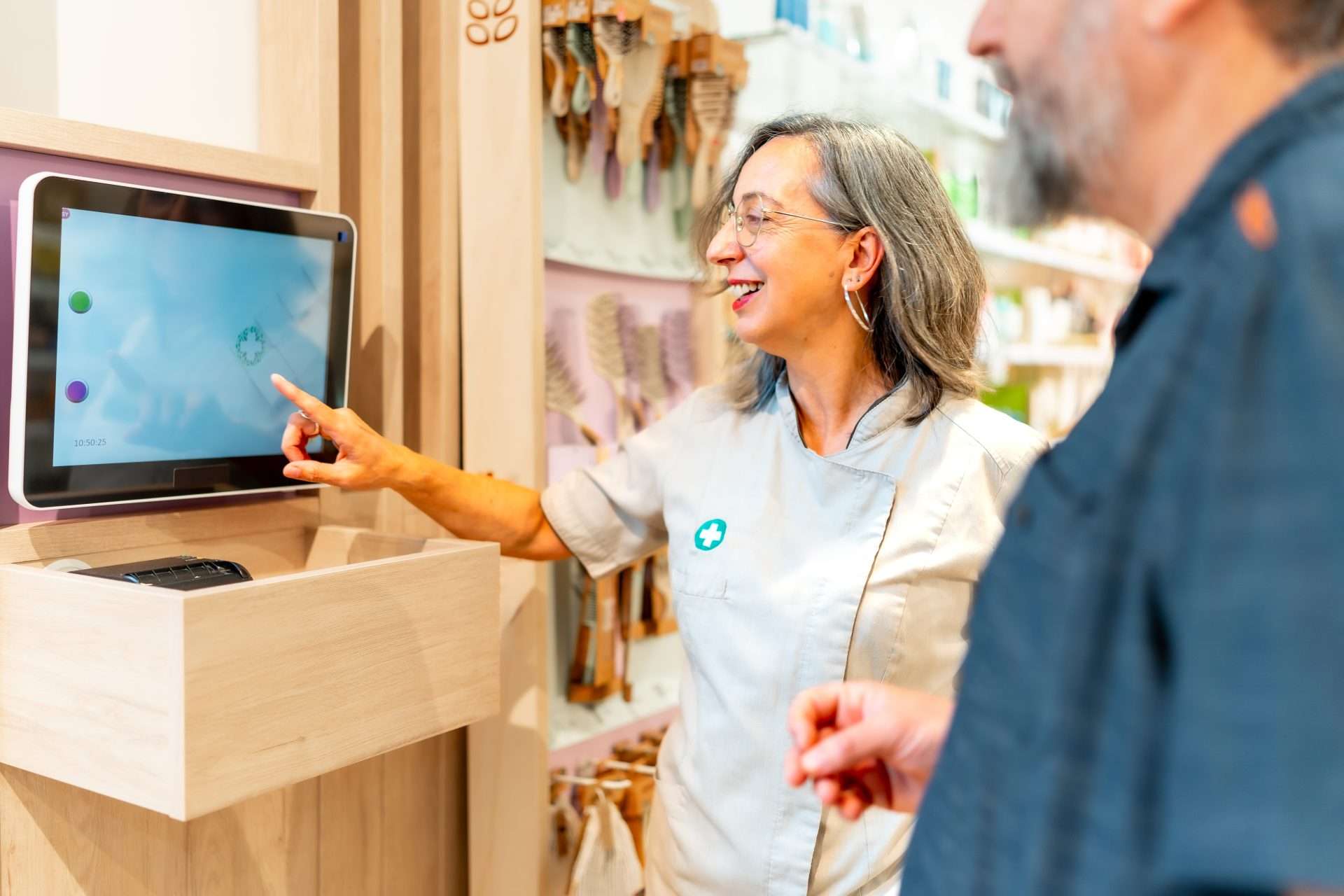 Smiling woman in a uniform points to a touchscreen kiosk, demonstrating custom software to a customer.