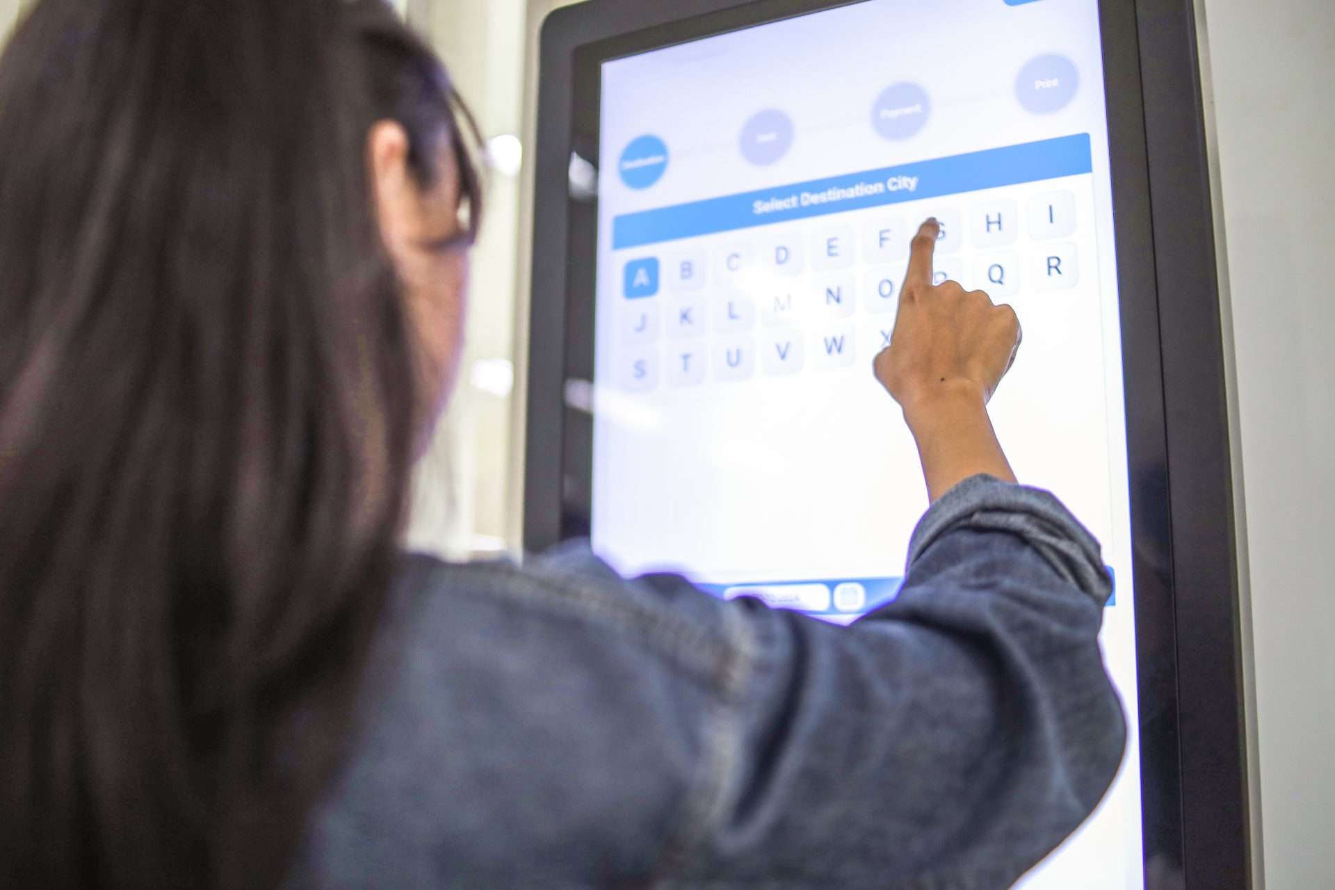 A person's hand touches a large, bright digital kiosk screen displaying a 
